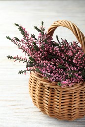 Heather branches with beautiful flowers in wicker basket on white wooden table