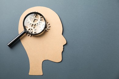 Amnesia. Human head cutout, cogwheels and magnifying glass on grey background, top view. Space for text