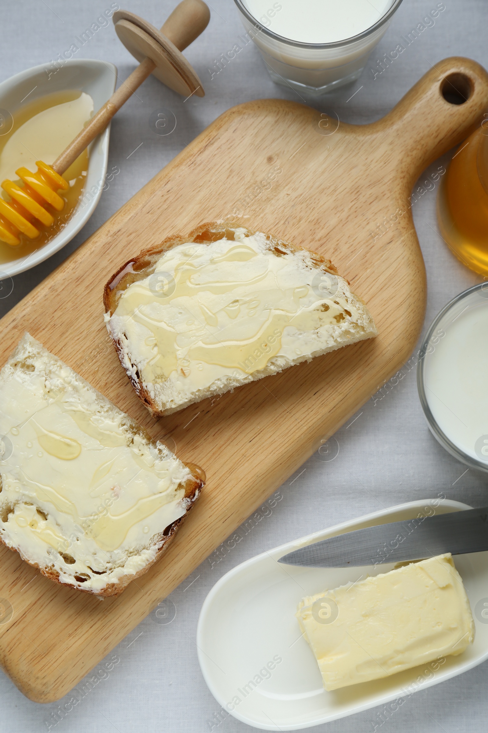 Photo of Slices of bread with butter, honey and milk on white table, flat lay