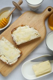 Slices of bread with butter, honey and milk on white table, flat lay