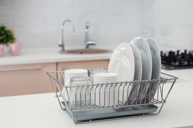 Photo of Dish drainer with clean dinnerware on table in kitchen