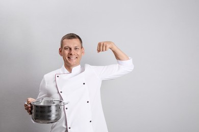 Photo of Happy male chef with cooking pot on light grey background. Space for text