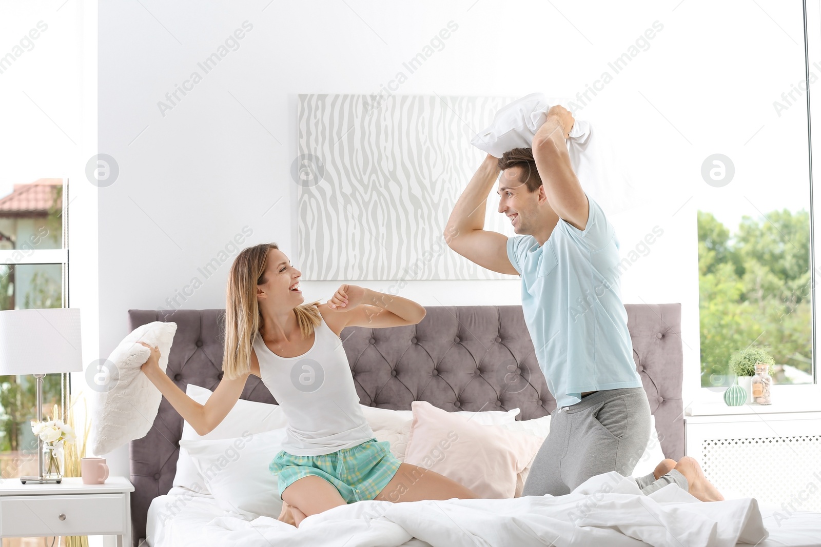 Photo of Young couple having pillow fight in bed at home