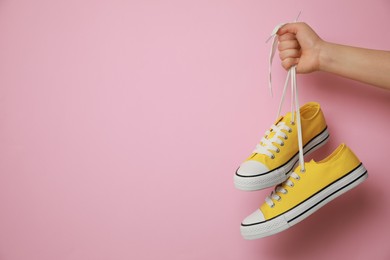 Photo of Woman holding pair of yellow classic old school sneakers on pink background, closeup. Space for text