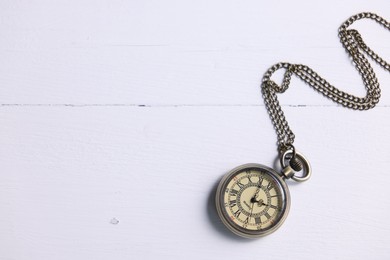 Photo of Pocket clock with chain on white wooden table, top view. Space for text