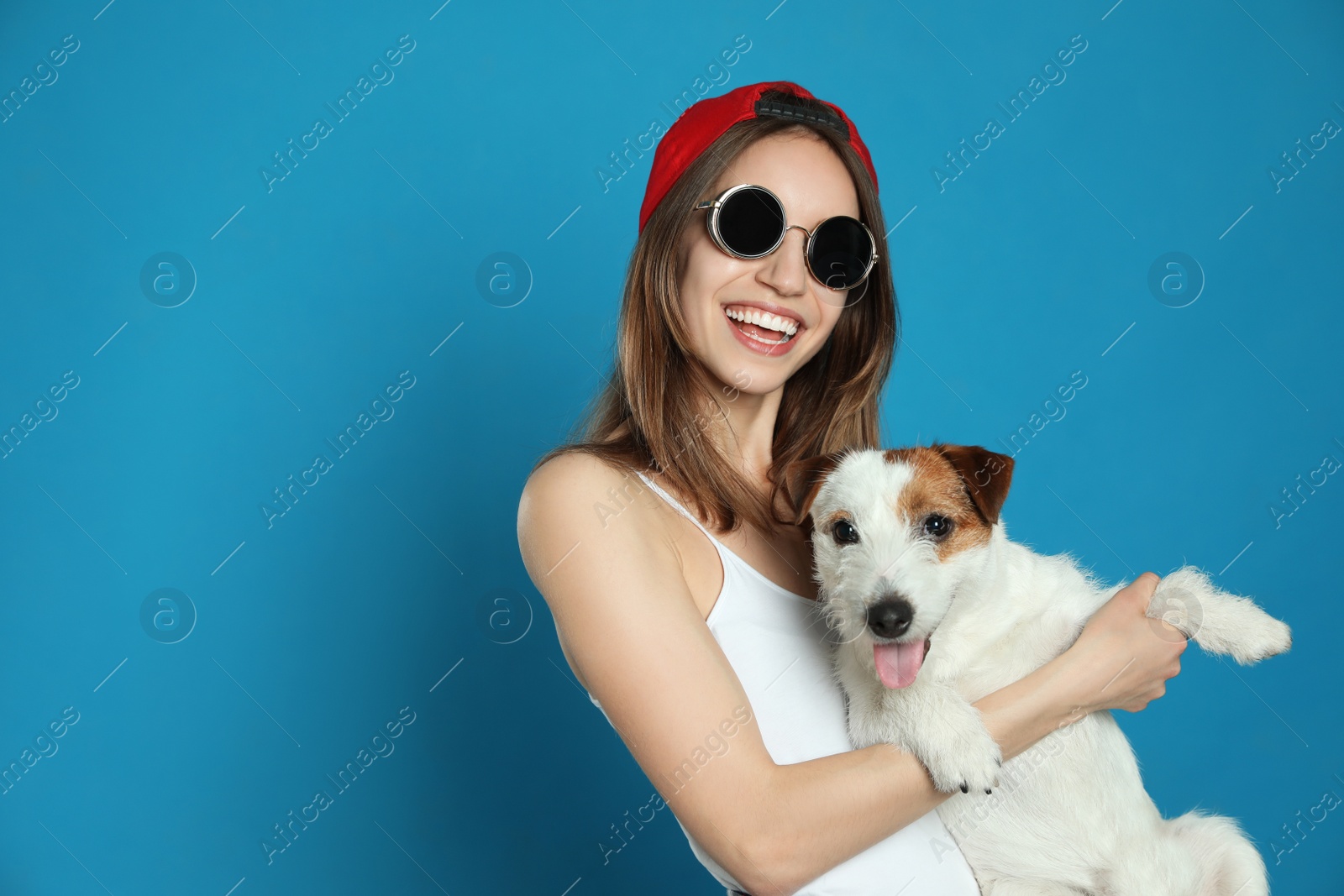 Photo of Young woman with her cute Jack Russell Terrier on light blue background, space for text. Lovely pet