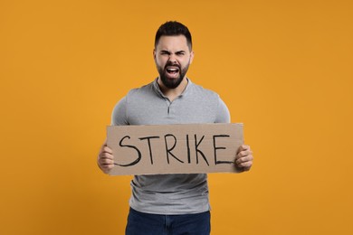 Photo of Angry man holding cardboard banner with word Strike on orange background
