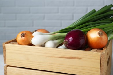 Photo of Wooden crate with different kinds of onions near white brick wall, closeup