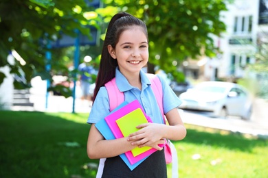 Cute little girl in school uniform with backpack and stationery on street