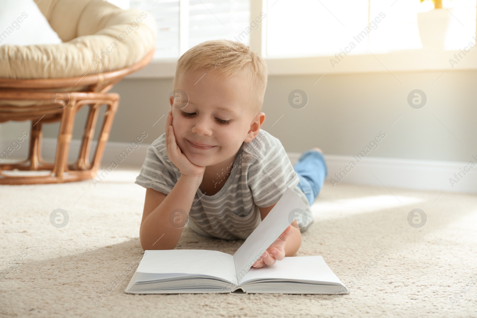 Photo of Cute little boy reading book on floor at home