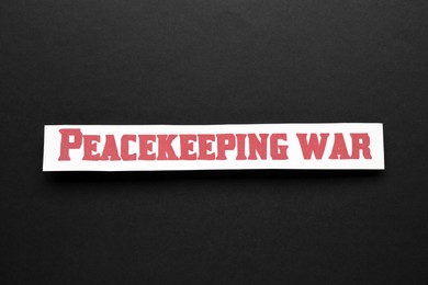 Photo of Paper with word Peacekeeping War on black background, top view