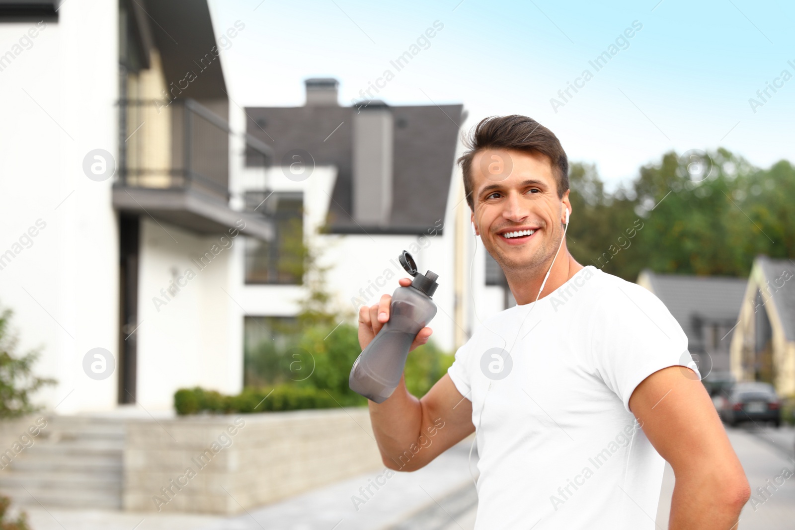 Photo of Young man with earphones drinking water after running on street. Healthy lifestyle