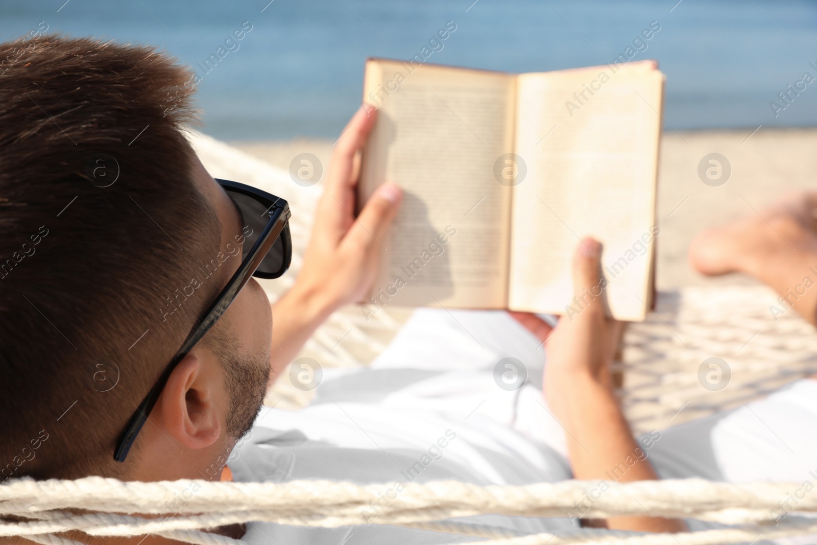 Photo of Young man reading book in hammock on beach