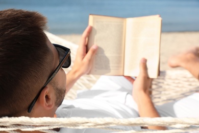 Young man reading book in hammock on beach