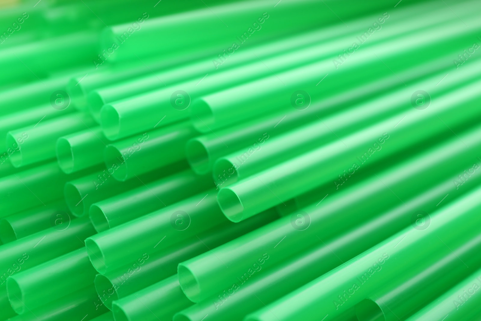 Photo of Heap of green plastic straws for drinks as background, closeup