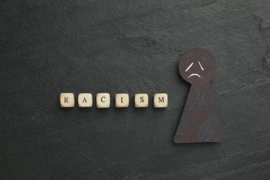 Photo of Word Racism and black paper figure with sad face on dark background, flat lay