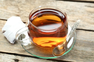 Photo of Aromatic tea in glass cup, spoon and teabags on wooden table