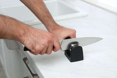 Photo of Man sharpening knife at white table indoors, closeup