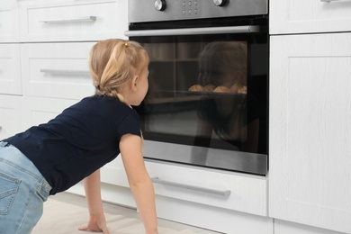 Little girl waiting for preparation of cookies in oven at home