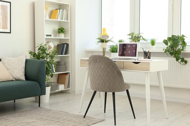 Photo of Cozy workspace with modern laptop on white wooden desk and comfortable chair at home