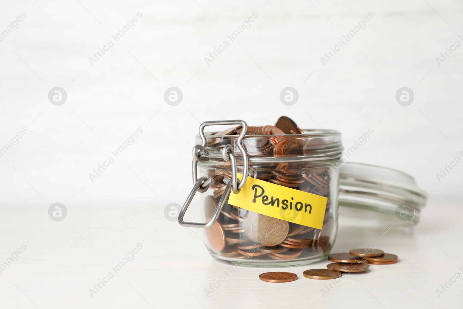 Photo of Coins in glass jar with label "PENSION" on table against light wall. Space for text