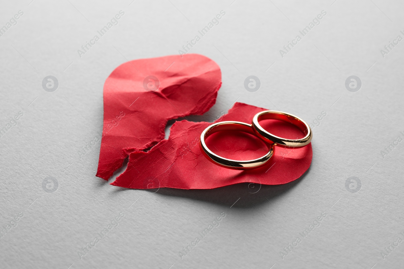 Photo of Halves of torn red paper heart and wedding rings on white background. Broken heart