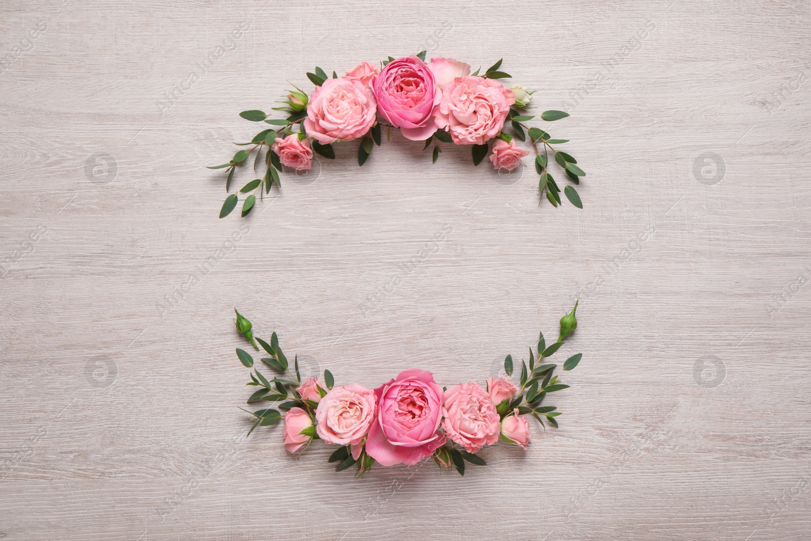 Photo of Wreath made of beautiful rose flowers and green leaves on white wooden background, flat lay. Space for text