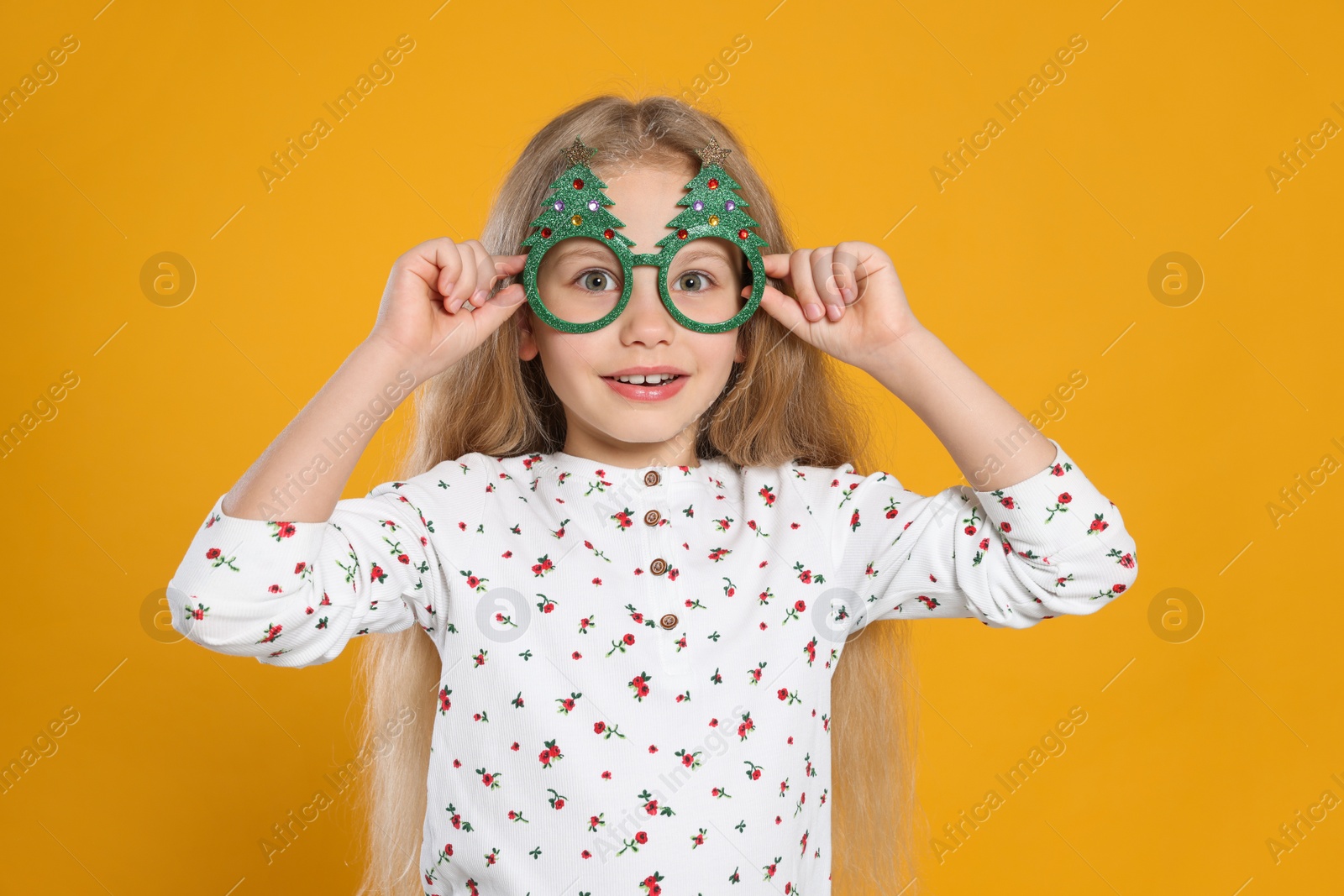 Photo of Smiling girl wearing decorative eyeglasses in shape of Christmas trees on orange background