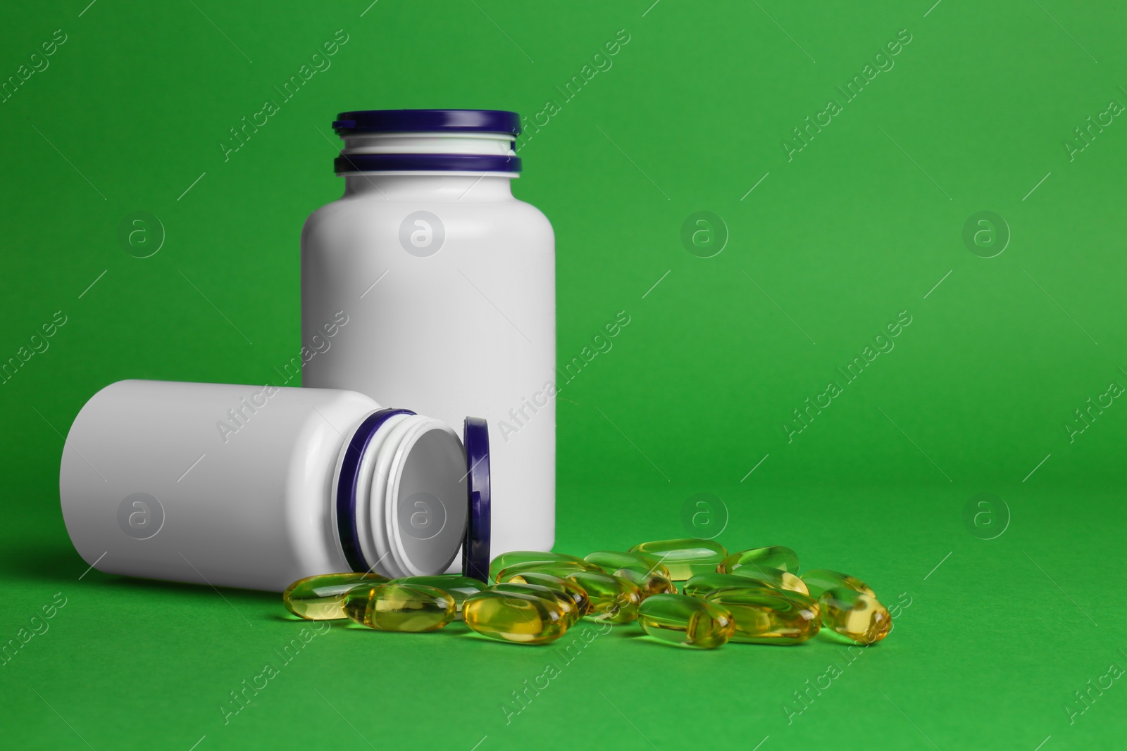 Photo of Plastic medicine bottles and scattered pills on green background, space for text. Medicament