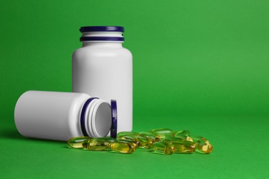 Plastic medicine bottles and scattered pills on green background, space for text. Medicament