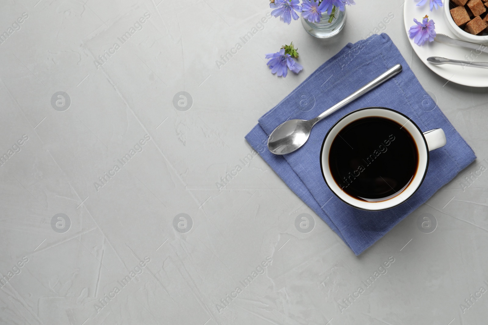 Photo of Cup of delicious chicory drink and flowers on light grey table, flat lay. Space for text