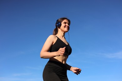 Young woman listening to music while running outdoors in morning, low angle view