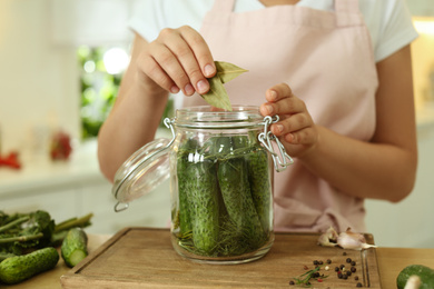 Photo of Woman putting bay leaves into pickling jar at table in kitchen, closeup