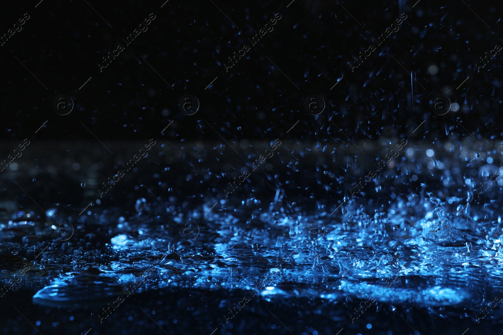 Photo of Heavy rain falling down on ground against dark background, toned in blue