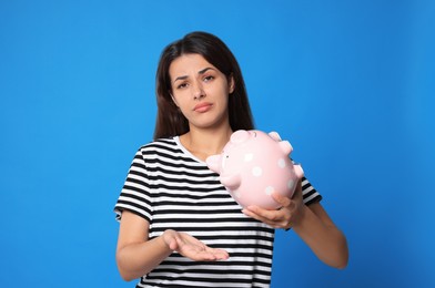 Photo of Confused young woman with empty piggy bank on light blue background