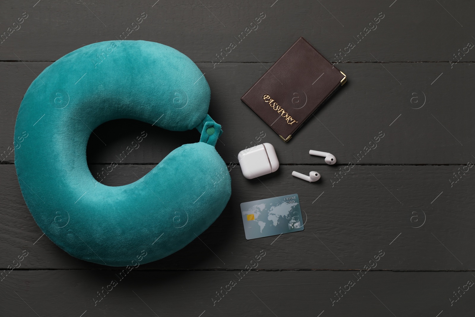 Photo of Turquoise travel pillow, passport, credit card and earphones on black wooden background, flat lay. Space for text