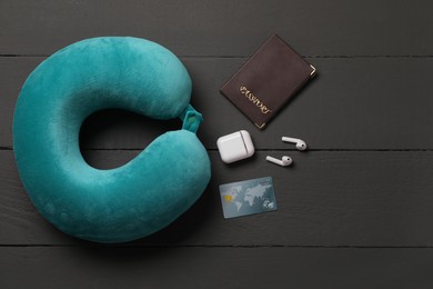 Photo of Turquoise travel pillow, passport, credit card and earphones on black wooden background, flat lay. Space for text