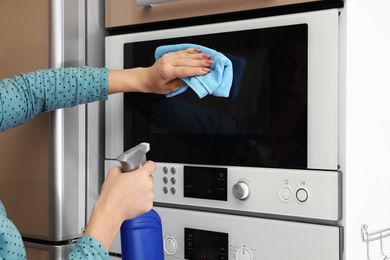 Photo of Woman cleaning oven with rag in kitchen