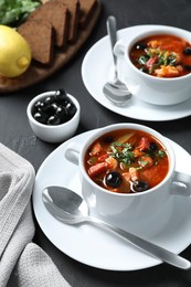 Photo of Meat solyanka soup with sausages and olives served on dark grey table