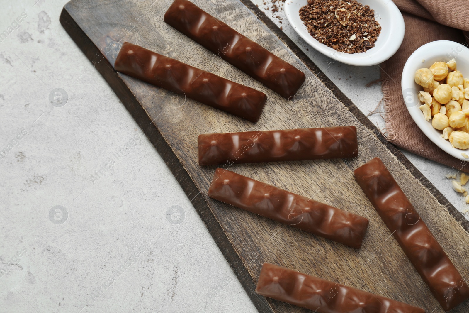 Photo of Tasty chocolate bars and nuts on light grey table, flat lay. Space for text