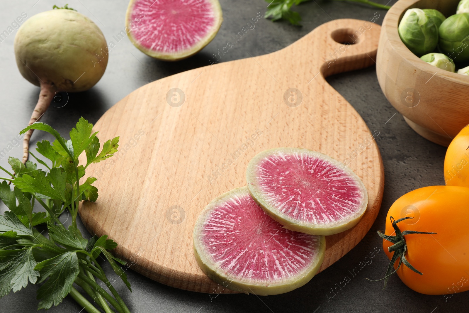 Photo of Wooden cutting board and products on dark textured table, closeup