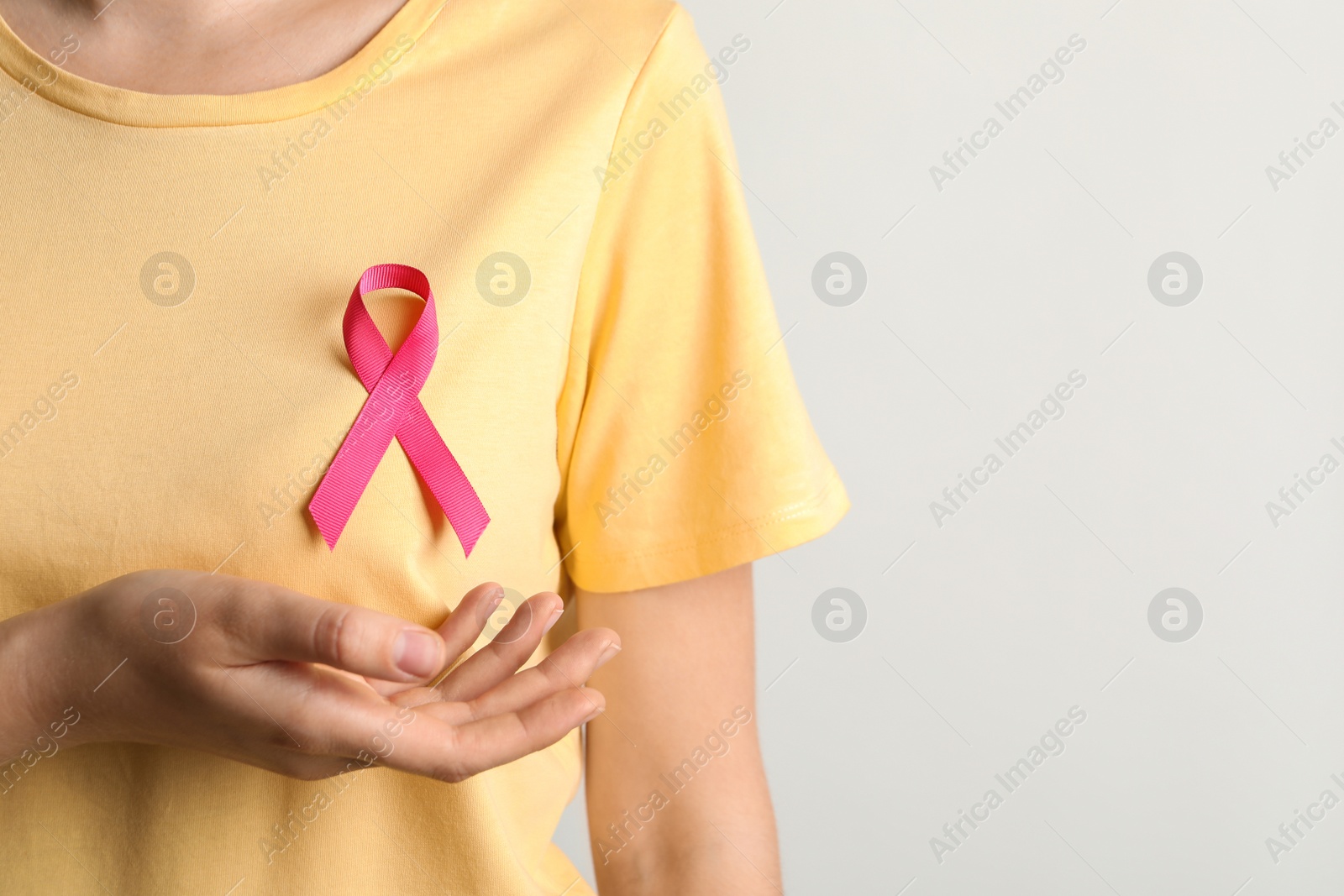 Photo of Woman with pink ribbon on t-shirt against light background. Cancer awareness