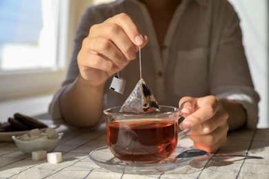 Woman taking tea bag out of cup at table indoors, closeup