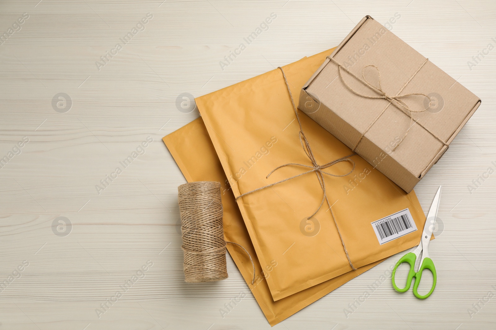 Photo of Padded envelopes, box, rope and scissors on white wooden background, flat lay. Space for text