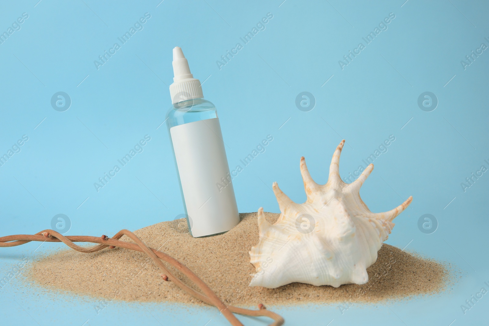 Photo of Bottle with serum, shell and branches on sand against light blue background. Cosmetic product