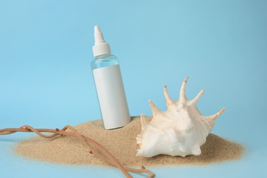 Bottle with serum, shell and branches on sand against light blue background. Cosmetic product