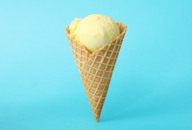 Photo of Delicious yellow ice cream in waffle cone on light blue background