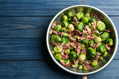 Delicious Brussels sprouts with bacon on blue wooden table, top view. Space for text