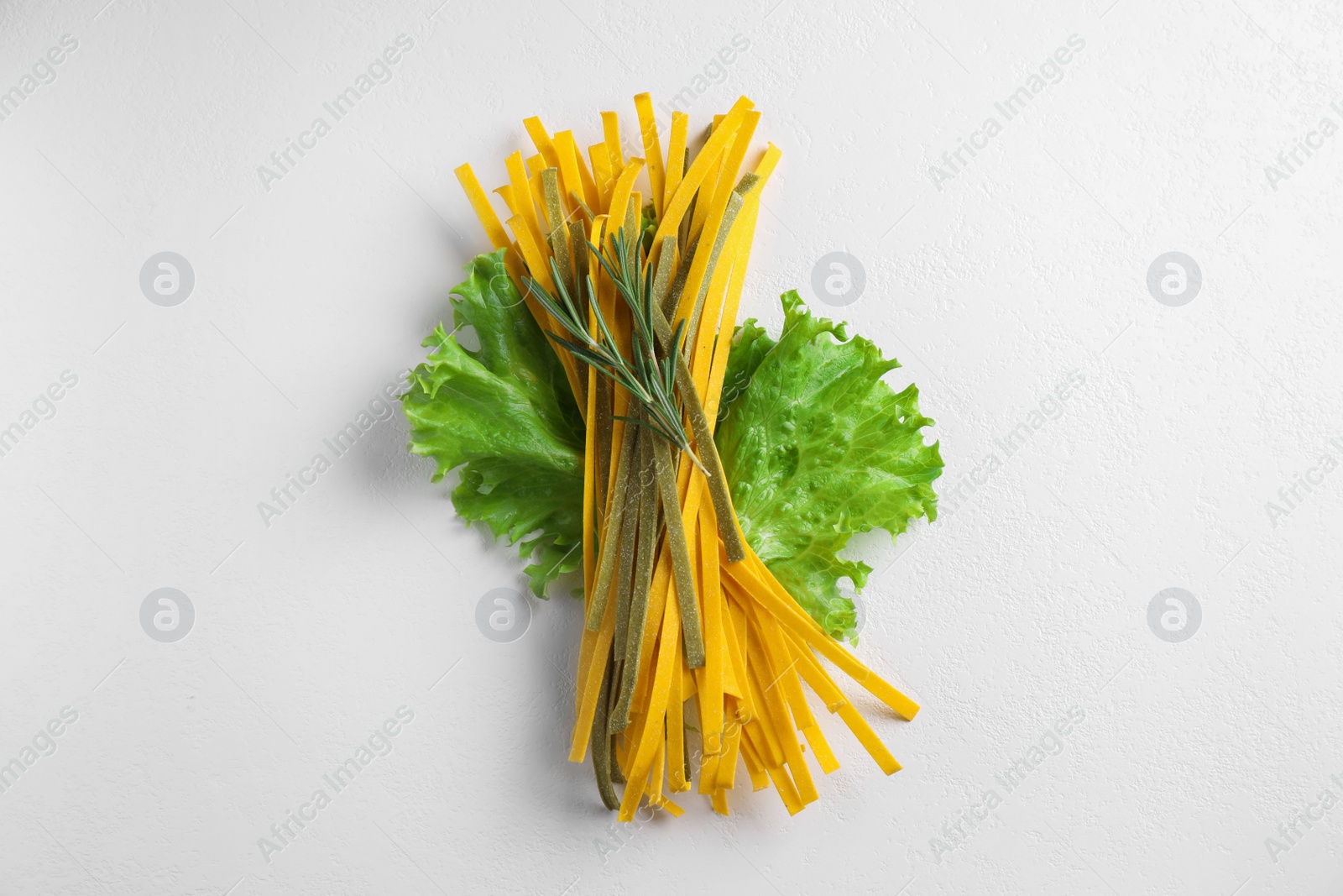 Photo of Uncooked spaghetti with rosemary and lettuce on white table, top view. Italian pasta