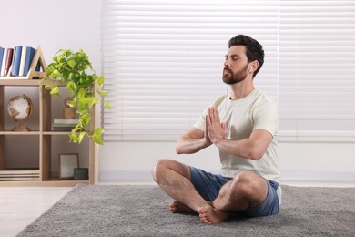 Photo of Man in earphones meditating at home, space for text